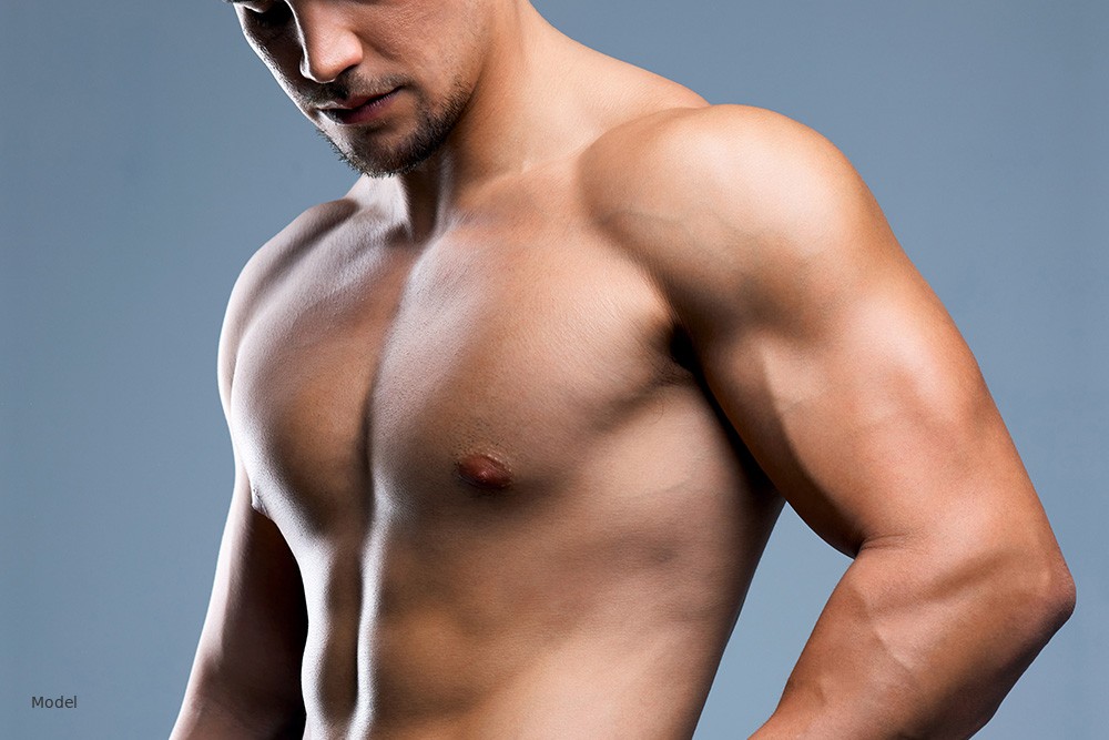 Fit male torso with defined chest, studio blue-gray background